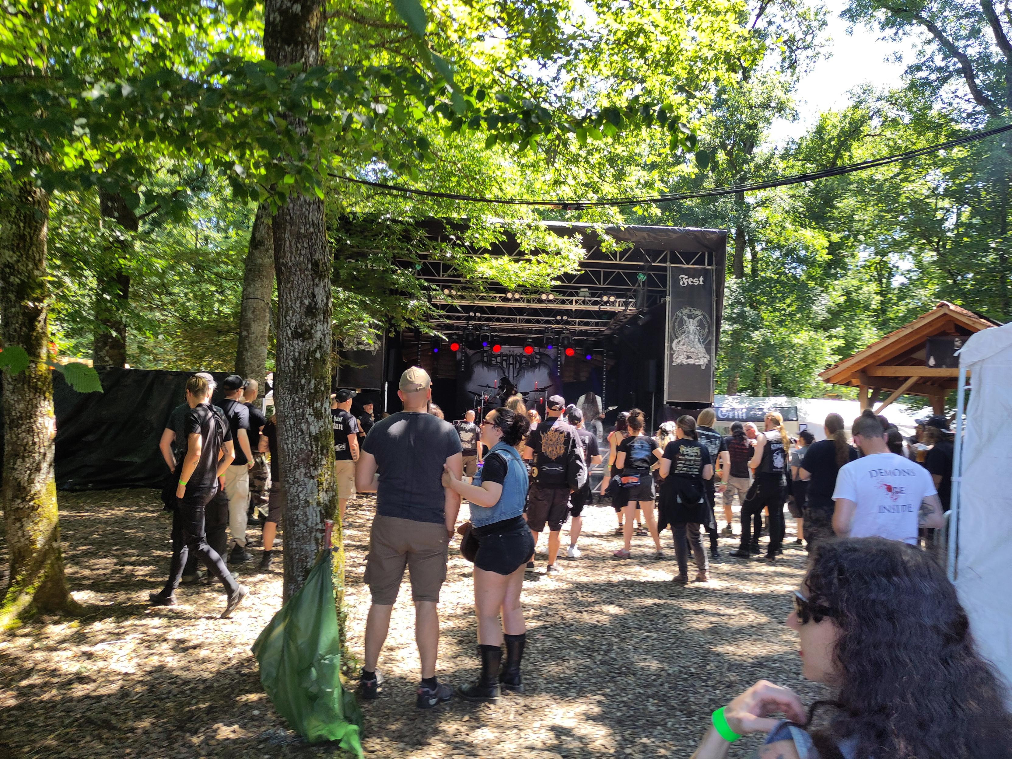 Small stage in a forest, a band is playing in front of a sparse audience